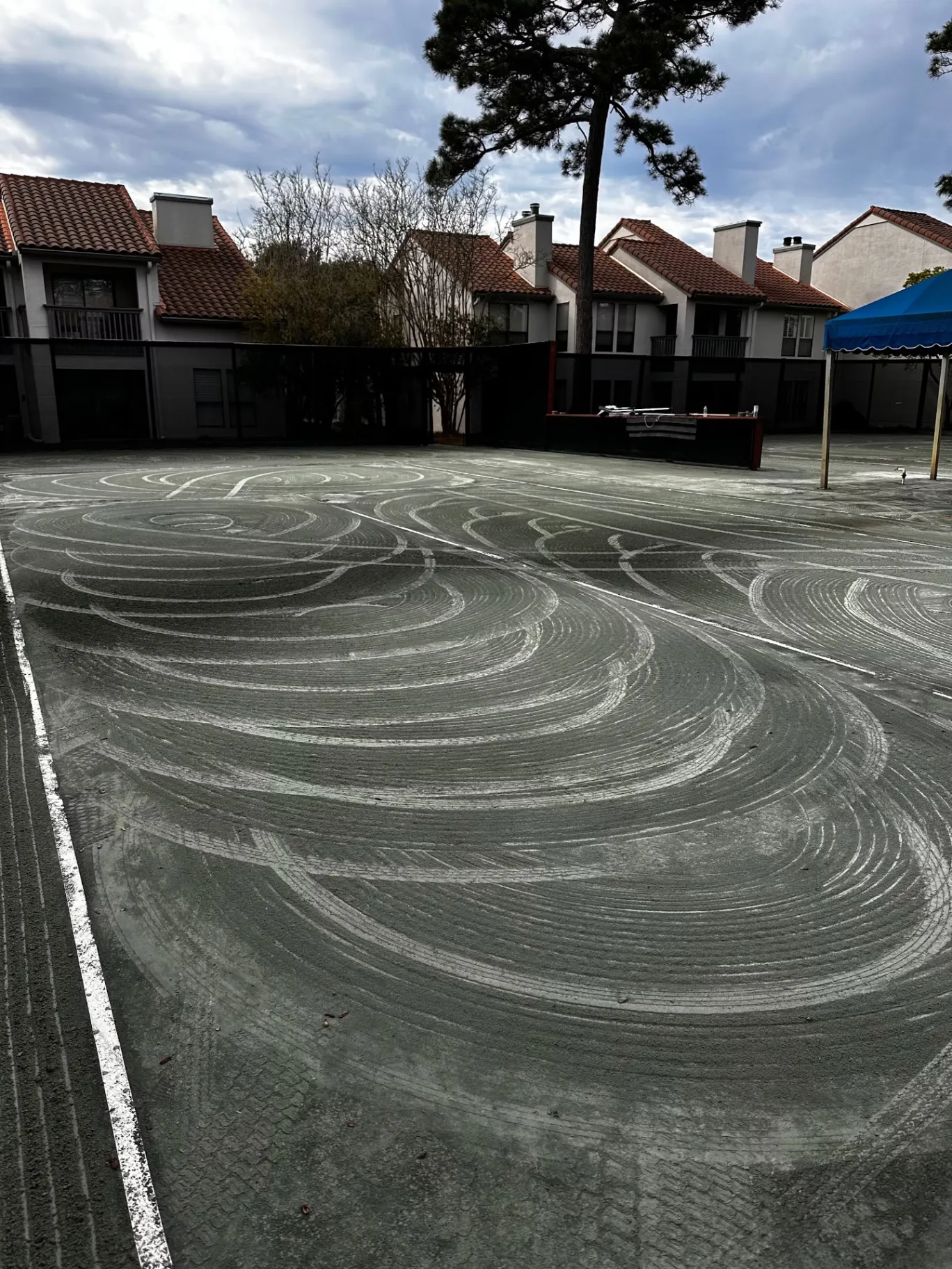 Circular working marks across a court surface near a blue canopy.