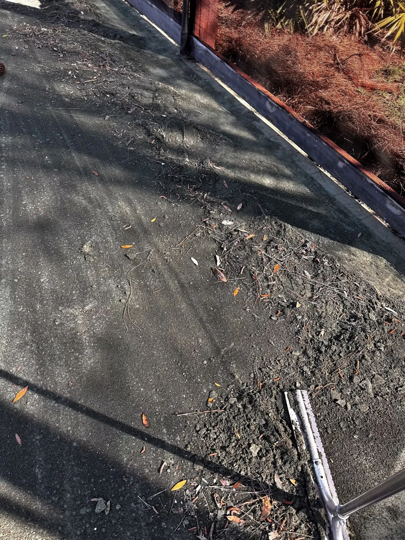 Loose court-surface material and debris along the perimeter beside a hand tool.